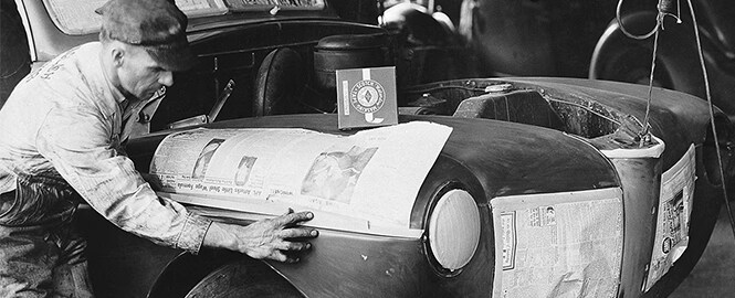 Zwart-wit afbeelding van een man die maskeertape gebruikt bij het spuiten van een auto
