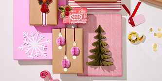 Kerstdecoraties en papieren knutselwerk zoals bomen en kerstballen bevestigd aan ingepakte geschenken met Scotch® Dubbelzijdige Tape
